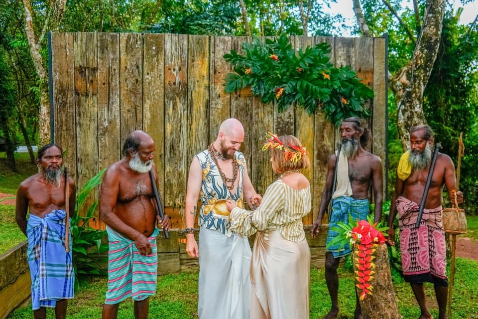 Couple exchanging vows before a rustic wooden backdrop surrounded by community elders
