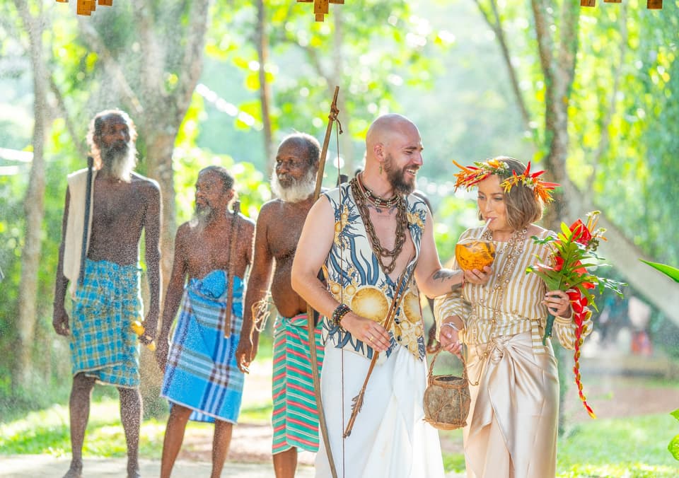 Couple and community elders walking in a sunlit procession through the forest