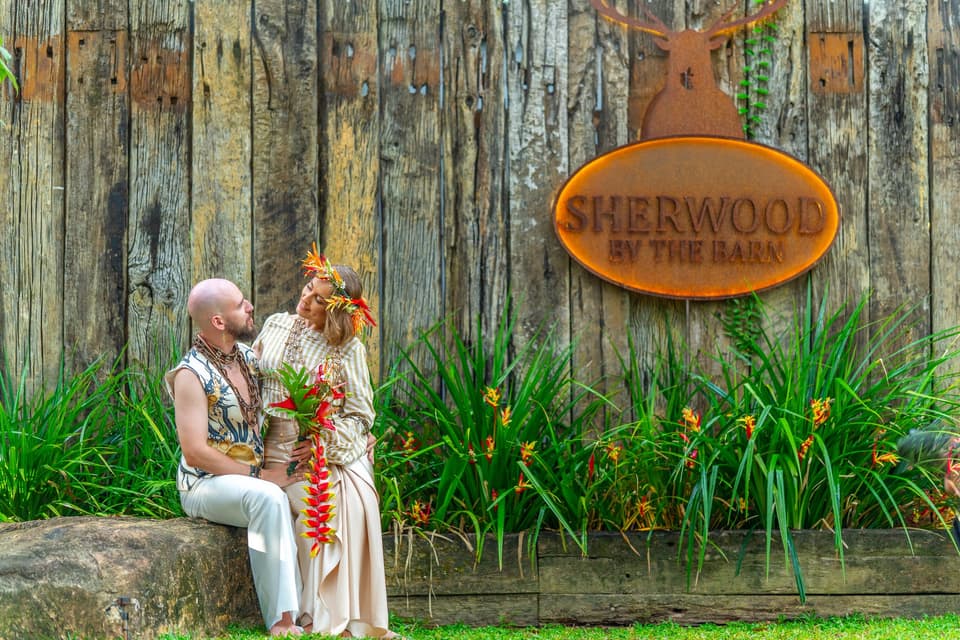 A couple standing at the Sherwood by The Barn entrance sign amid lush forest greenery